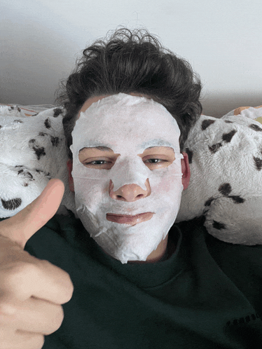 a young man with a white mask on his face gives a thumbs up