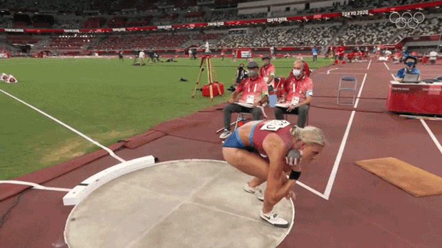 a female athlete is about to throw a discus in a stadium that says tokyo 2020