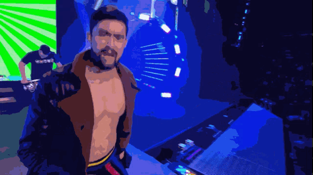 a man without a shirt is standing in a dark room with a green and blue background