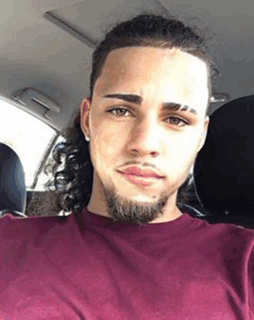 a young man with long hair and a beard is sitting in a car taking a selfie .