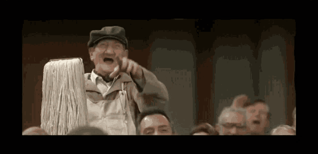 a man is holding a mop and pointing at the camera while a crowd watches .