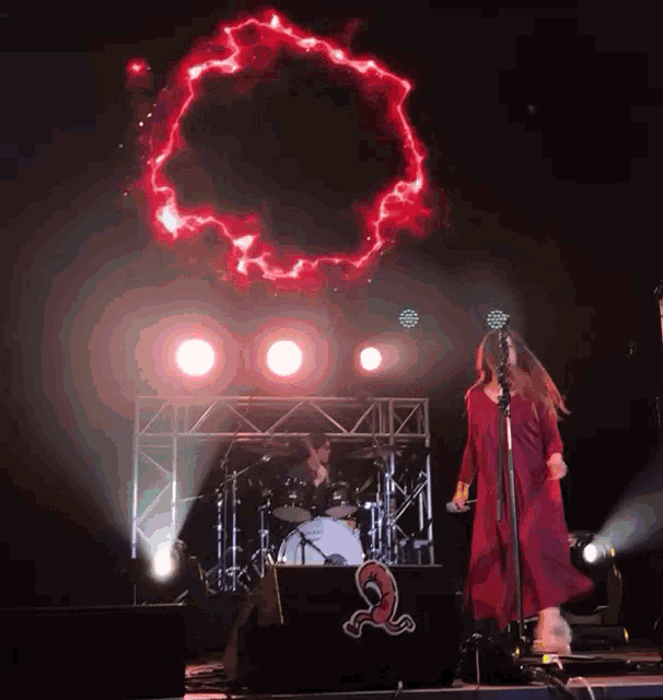 a woman in a red dress sings into a microphone in front of a drummer