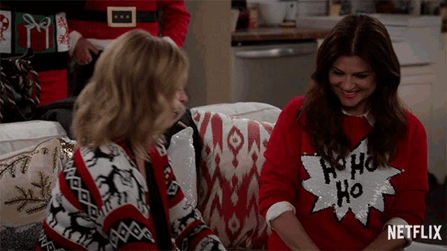 two women are sitting on a couch and one has a sweater that says ho ho ho