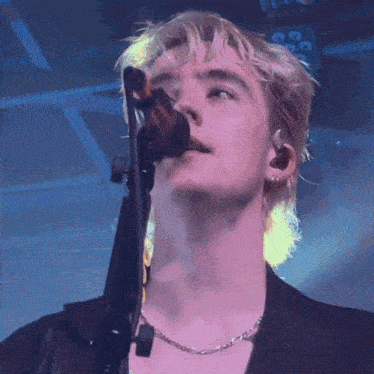 a man singing into a microphone while wearing a necklace