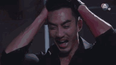 a man in a black shirt is holding his head in his hands .