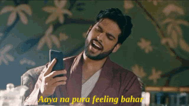 a man with a beard is laughing while looking at his phone with the words aaya na pura feeling bahar below him