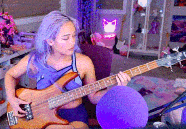a woman with purple hair is playing a guitar