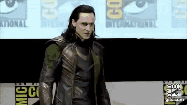 a man in a loki costume is standing in front of a screen at a convention .