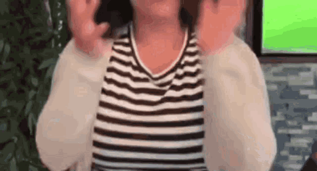 a woman in a striped shirt is making a funny face while standing in front of a green screen .