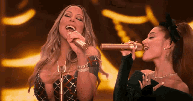 mariah carey and ariana grande singing into microphones on a stage
