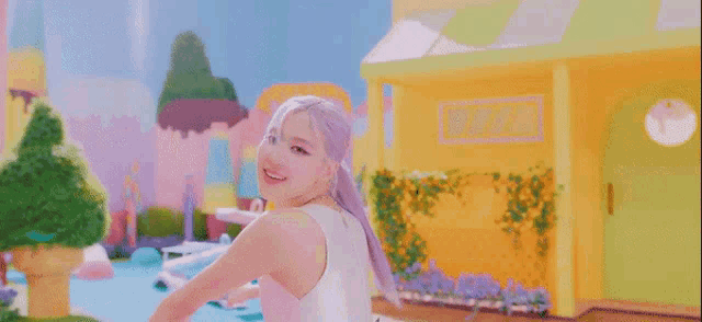 a woman in a white tank top is standing in front of a yellow building and smiling .