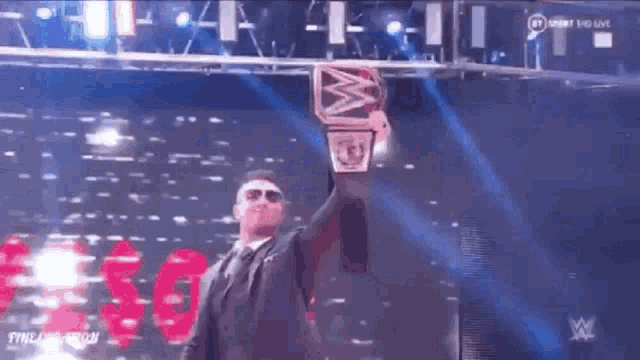 a man in a suit is holding up a wrestling championship belt .