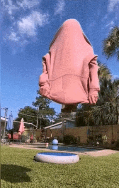 a person wearing a pink hoodie is floating in the air near a pool