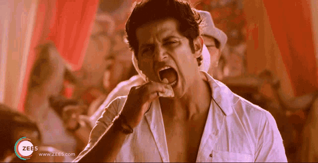 a man in a white shirt is eating a piece of food with a zee5 logo on the bottom