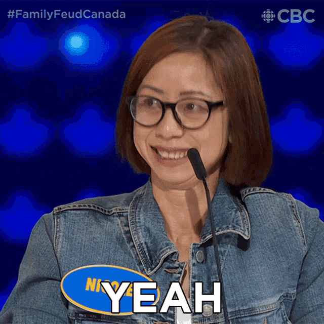 a woman wearing glasses and a denim jacket says " yeah " in front of a microphone