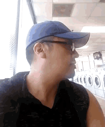 a man wearing glasses and a blue hat is standing in front of a laundromat