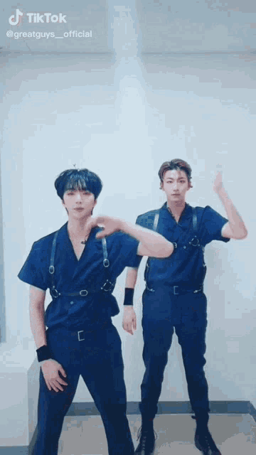two young men in blue jumpsuits are standing next to each other and dancing .