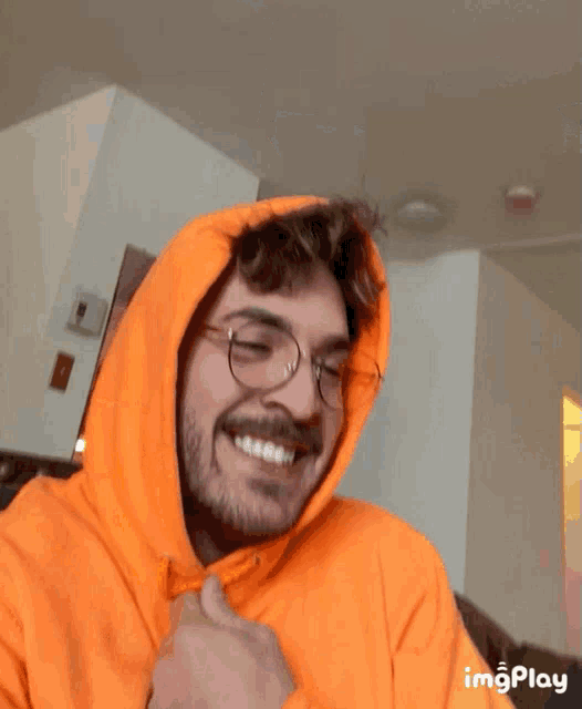a man wearing glasses and an orange hoodie smiles