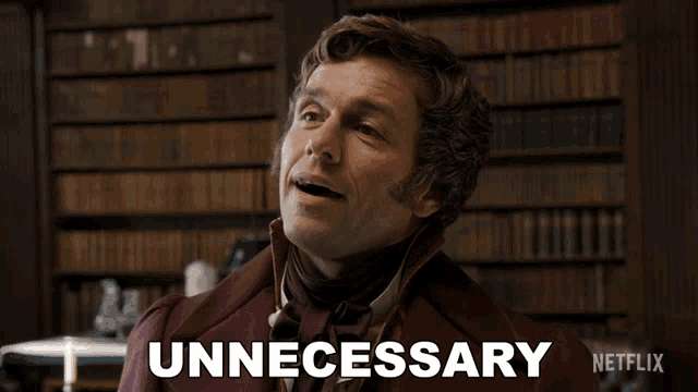 a man in a burgundy suit says unnecessary in front of a bookshelf