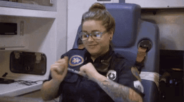a female paramedic is sitting in an ambulance and smiling while wearing a mask .