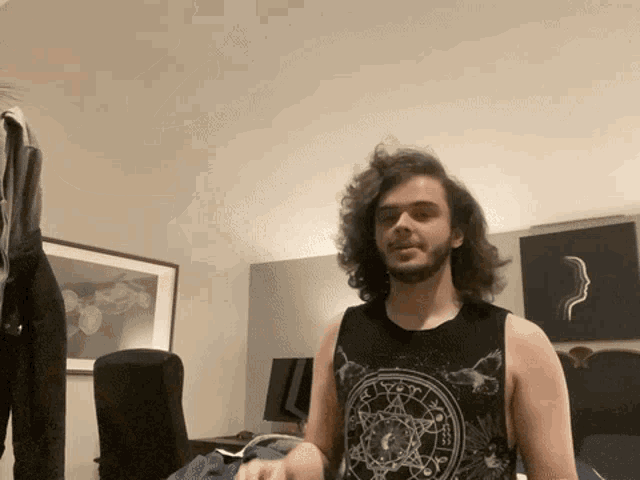 a man with long hair and a beard wears a black tank top with a circle on it