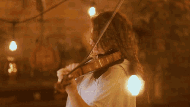 a woman is playing a violin in a dark room with lights hanging from the ceiling