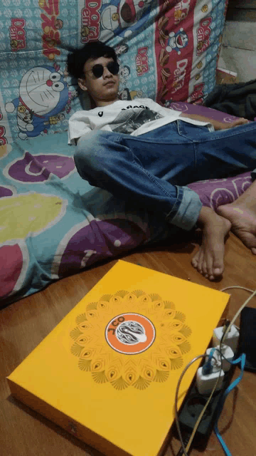 a boy wearing sunglasses is laying on a bed with a doraemon blanket on it