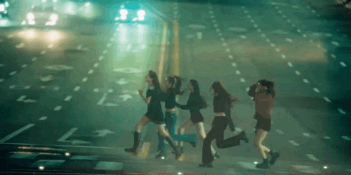 a group of young women are running down a street at night .