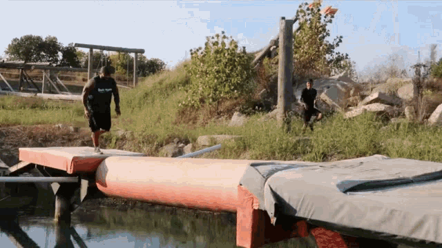 a man wearing a shirt that says ' best sport ' on it jumps over a body of water