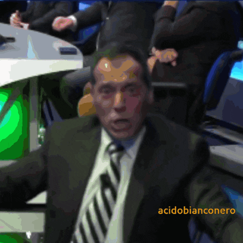 a man in a suit and tie is sitting in front of a green screen that says acidobianconero on it