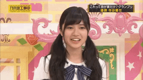 a girl with pigtails and a bow tie is smiling in front of a pink background .