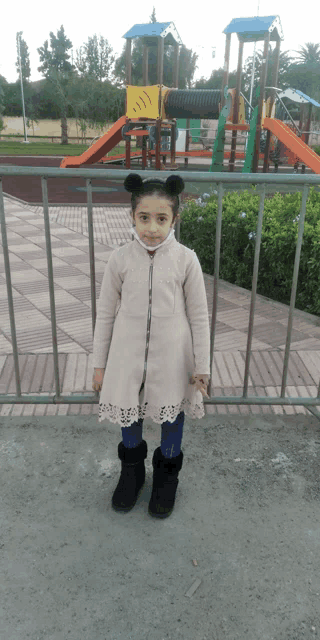 a little girl standing in front of a playground wearing a mask