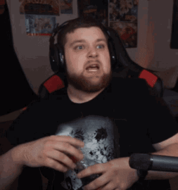 a man with a beard wearing headphones and a black shirt is sitting in front of a microphone