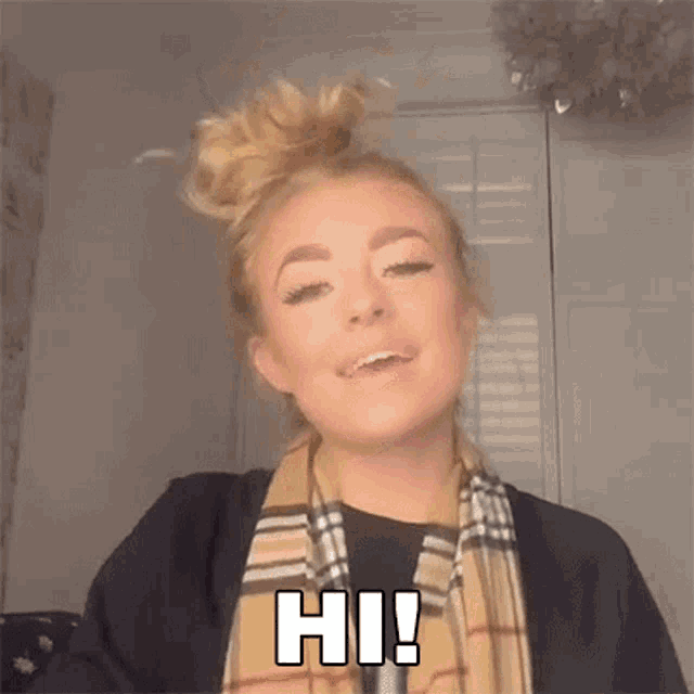 a woman wearing a plaid scarf and a bun says hi