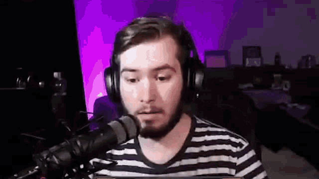 a man with a beard is sitting in front of a microphone wearing headphones and a striped shirt .