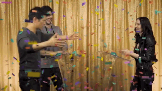 a group of people are standing in front of a curtain with confetti falling around them