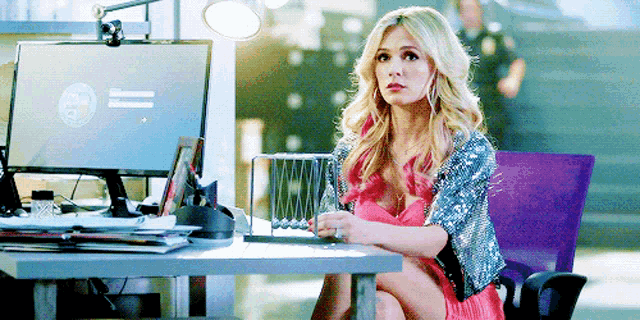 a woman in a pink dress sits at a desk in front of a computer monitor that has the letters ic on it