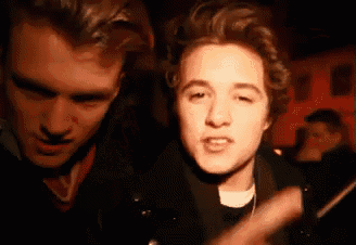 two young men are standing next to each other in a dark room and one of them is making a funny face