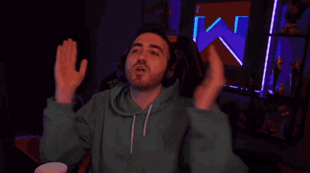 a man in a green hoodie is sitting in front of a screen with the letter m on it