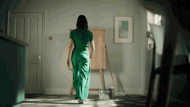 a woman in a green dress is walking in a room with a mop and bucket
