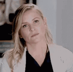 a close up of a woman 's face wearing a white lab coat and a black shirt .