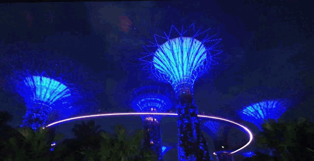 a bridge surrounded by trees with purple lights and a sign that says " gardens by the bay "