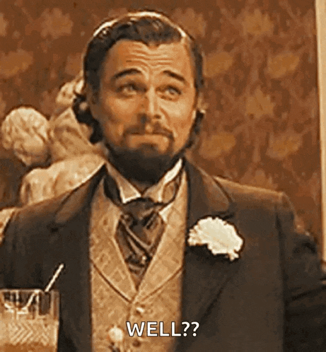 a man in a suit and tie is holding a glass of whiskey and asking , `` well ? ''