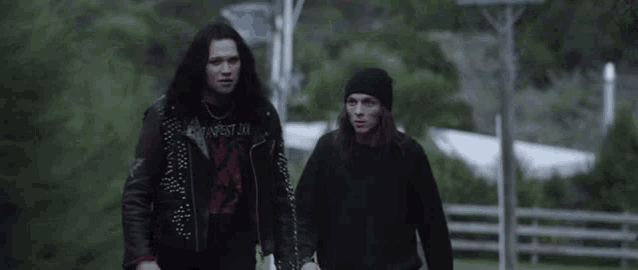 two men are walking down a street and one of them is wearing a t-shirt that says harvest
