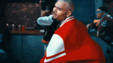 a man in a red and white varsity jacket is standing in front of a group of people .