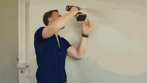 a man in a blue shirt is using a drill to fix a hole in a wall