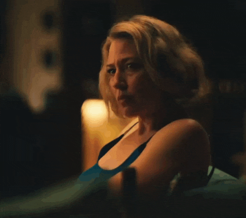 a woman in a blue tank top is sitting in a dark room with a bottle of beer in her hand .