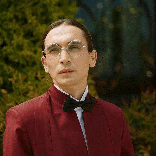 a man wearing glasses and a bow tie is wearing a red suit