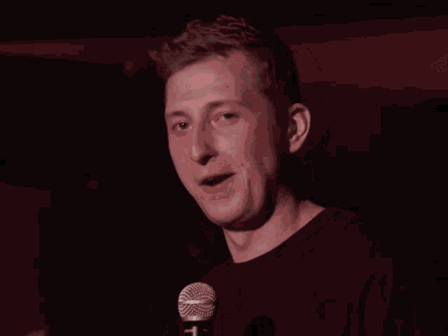 a man in a black shirt is laughing while holding his nose in front of a shure microphone
