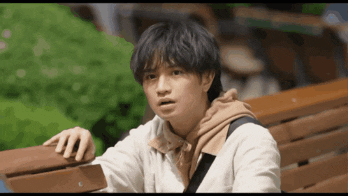 a young man is sitting on a wooden bench with his hand on the railing